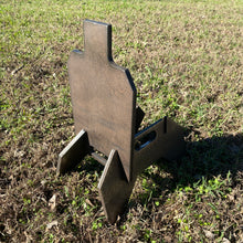 Load image into Gallery viewer, A 7inx12in 3/8in AR500 steel shooting target in the shape of an IDPA silhouette placed on a 3/8in AR500 metal ground stand on grass.