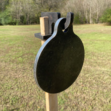 Load image into Gallery viewer, A 6in 3/8in AR500 steel shooting target with a 1x2 hook for mounting on 1x2 wood, placed outdoors with grassy background.