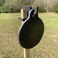 A 6in 3/8in AR500 steel shooting target with a 1x2 hook for mounting on 1x2 wood, placed outdoors with grassy background.