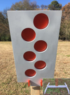 A 12inx24in 3/8in AR500 white and orange steel shooting target with interlocking swinging paddles, accompanied by a 2x4 mount and stand, set outdoors.