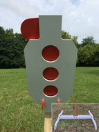 A 13inx30in 3/8in AR500 white and orange steel shooting target with interlocking swinging paddles, accompanied by a 2x4 mount and stand, set outdoors.